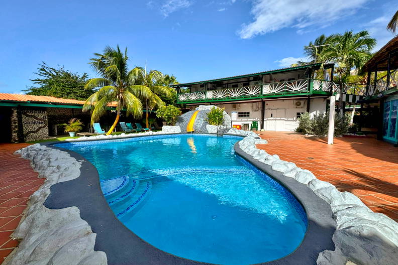 Basen otoczony palmami i budynkami w słoneczny dzień.