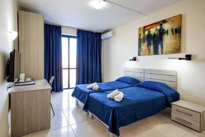 Pokój hotelowy z dwoma łóżkami w niebieskiej pościeli i obrazem na ścianie.