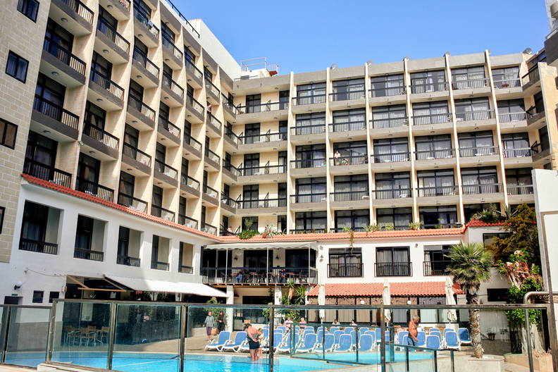 Hotel z basenem pełnym ludzi w słoneczny dzień.