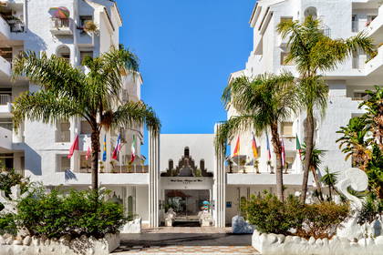 Hotel Suites Albargin del Mar z palmami i flagami powiewającymi na wietrze.