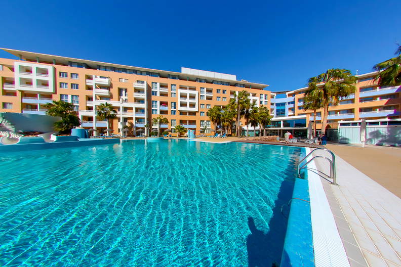 Basen w kurorcie z palmami, w tle budynek.