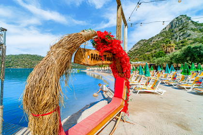 Wejście na Paradise Beach: łuk ze słomy i kwiatów, plaża z leżakami oraz góry w tle.