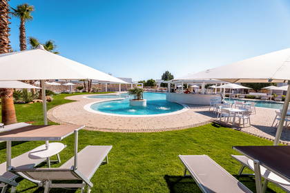 Basen otoczony leżakami i palmami.