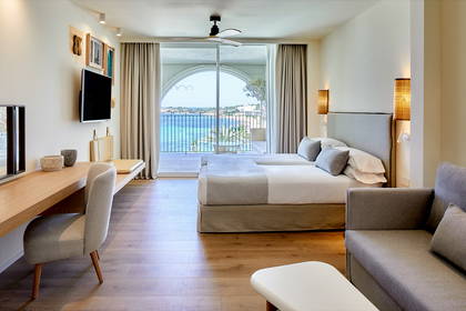 Jasny pokój hotelowy z balkonem i widokiem na morze.