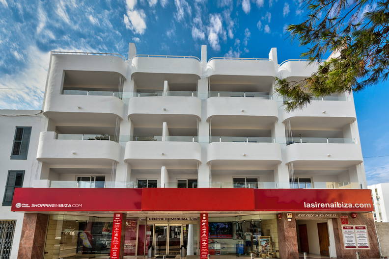 Trzypiętrowy, biały budynek z czerwonym szyldem reklamowym na parterze.