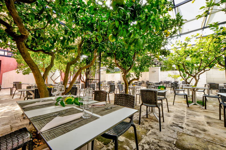 Restauracja na świeżym powietrzu z drzewami owocowymi i zastawionymi stołami.