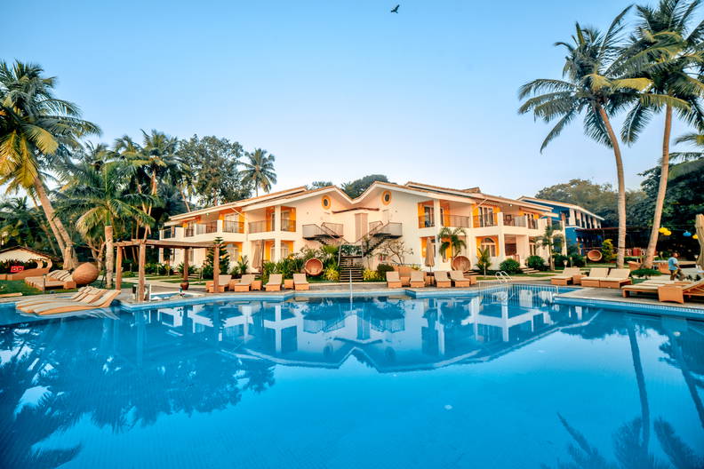 Hotel z basenem i palmami w słoneczny dzień.