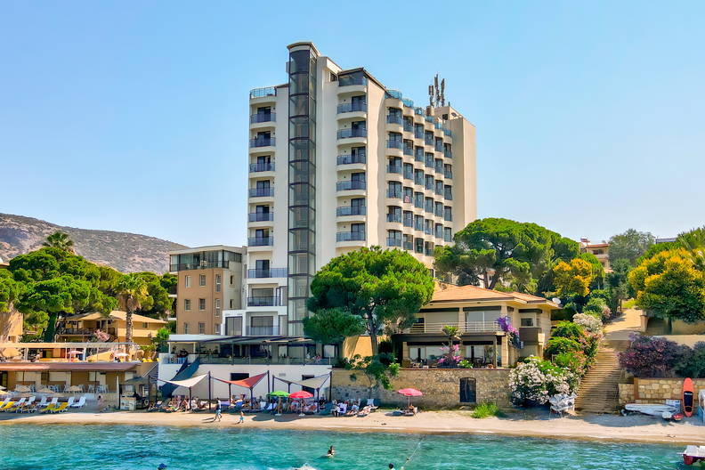 Hotel przy plaży z wieżowcem w tle i błękitna woda.