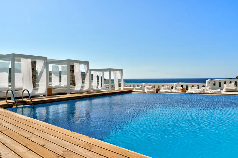 Basen z drewnianym tarasem i białymi leżakami z widokiem na morze.