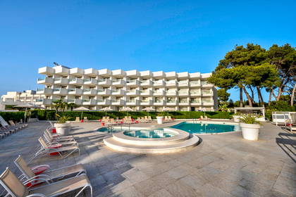 Biały hotel z basenem i leżakami.