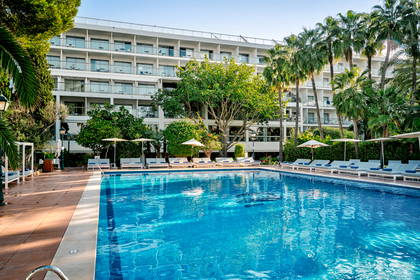 Basen z leżakami i palmami przy hotelu.