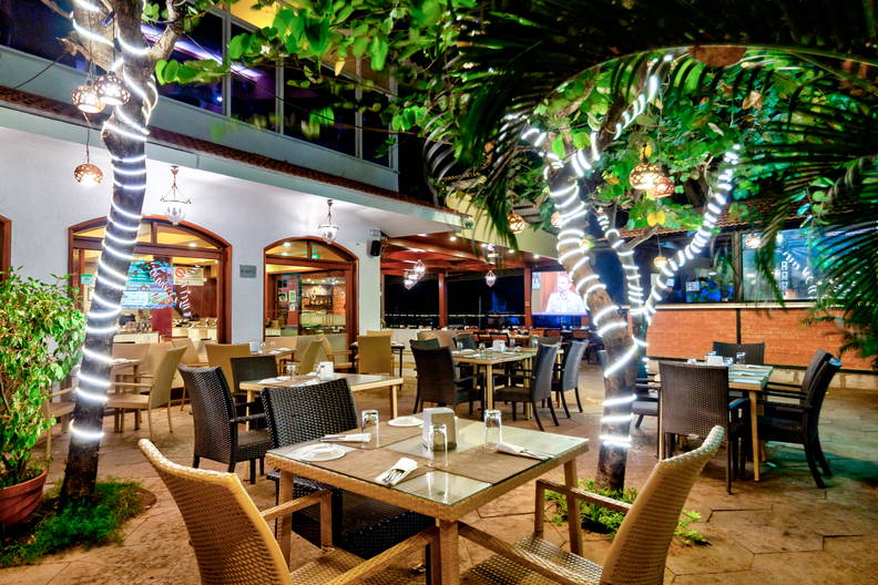 Restauracja na zewnątrz z oświetlonymi drzewami i stolikami.