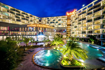 Oświetlony nocą hotel Muong Thanh Phu Quoc z basenem i palmami.