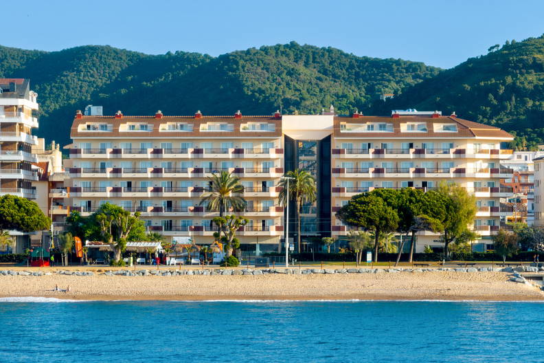 Hotel na plaży z błękitną wodą. W tle zalesione wzgórza.