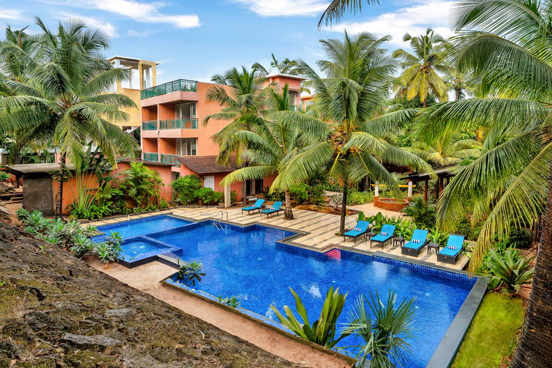 Kompleks hotelowy z basenem otoczonym palmami.