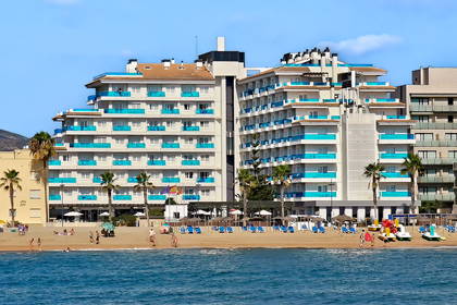 Hotel na plaży z palmami i wczasowiczami.