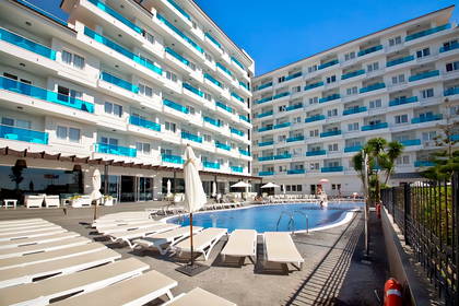 Kompleks hotelowy z basenem i leżakami w słoneczny dzień.