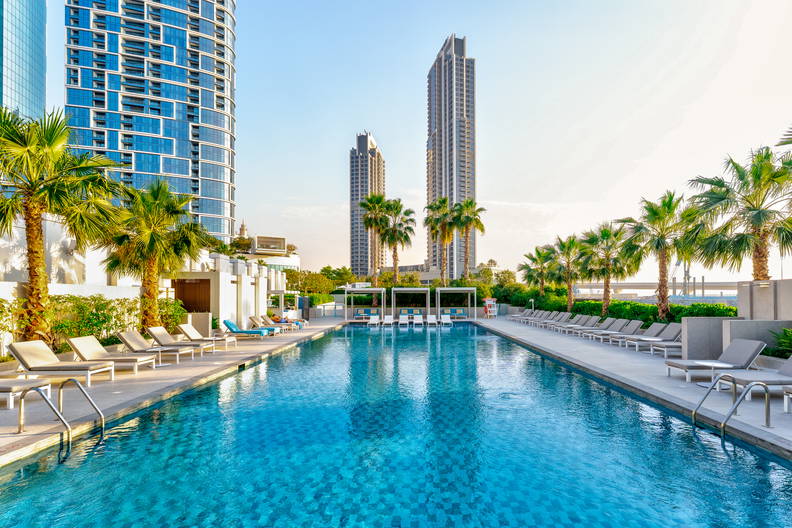 Basen z leżakami i palmami na tle miasta.