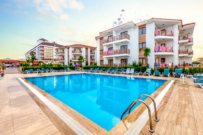 Basen hotelowy z leżakami i budynkami w tle.
