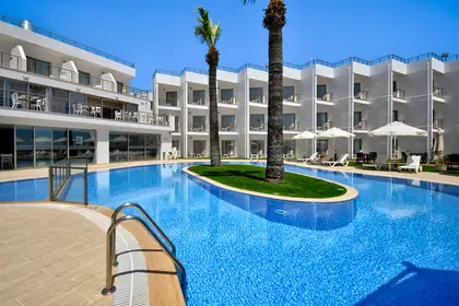 Hotel z basenem i palmami w słoneczny dzień.