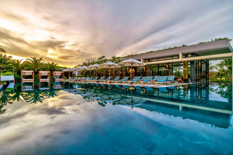 Basen z leżakami i parasolami, którego odbicie lustrzane widać w wodzie.