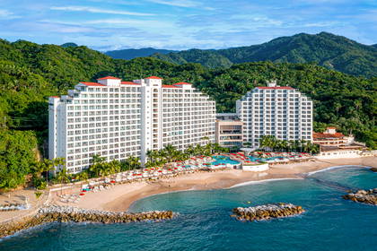 Hotel z plażą nad oceanem, w tle zielone wzgórza.