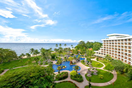 Hotel z basenami i palmami widziany z góry. W tle ocean.