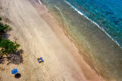 Plaża z lotu ptaka: leżaki i parasol.
