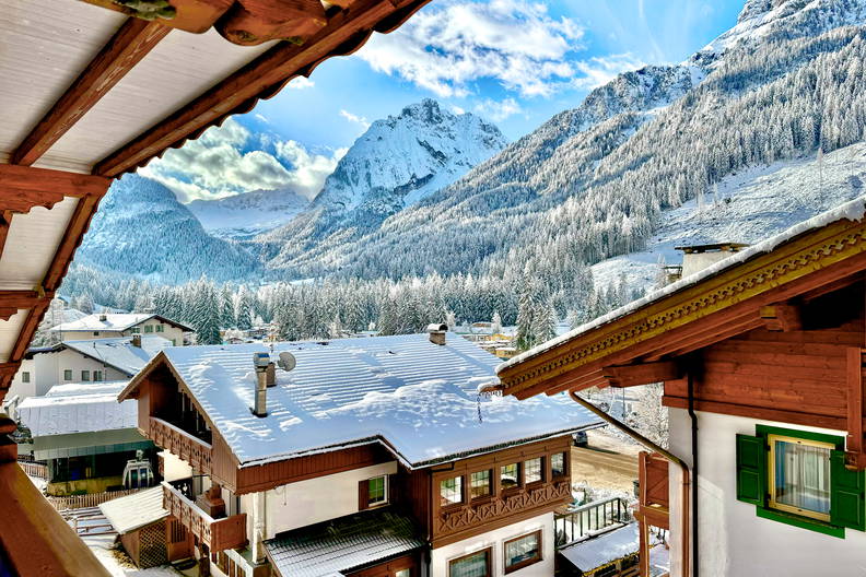 Widok z balkonu na ośnieżone domy i góry w oddali.