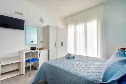 Jasny pokój hotelowy z łóżkiem, biurkiem i telewizorem.