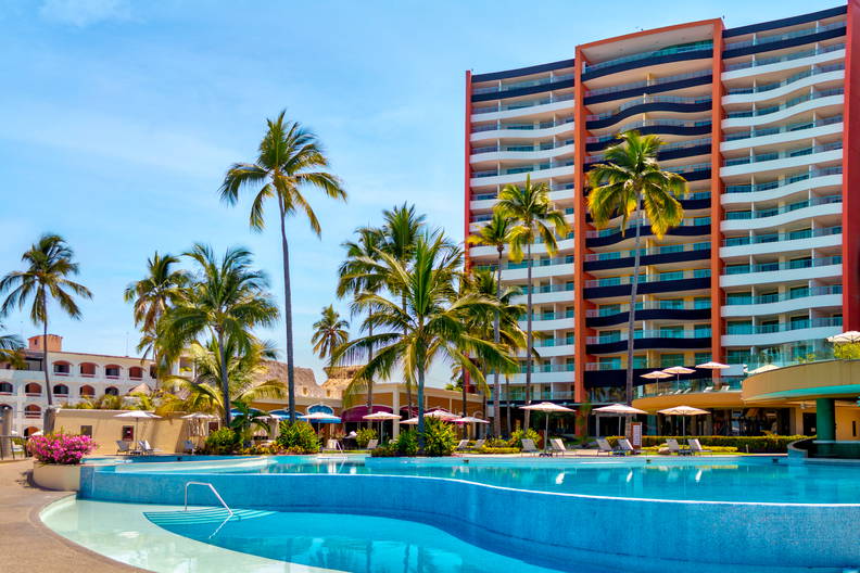 Hotel z basenem i palmami w słoneczny dzień.