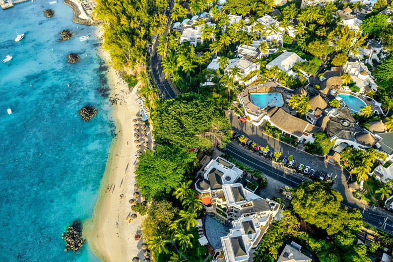 Tropikalna plaża z lotu ptaka: turkusowa woda, biały piasek, palmy i luksusowe kurorty.