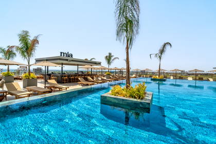 Basen z leżakami i bar hotelowy w tle.