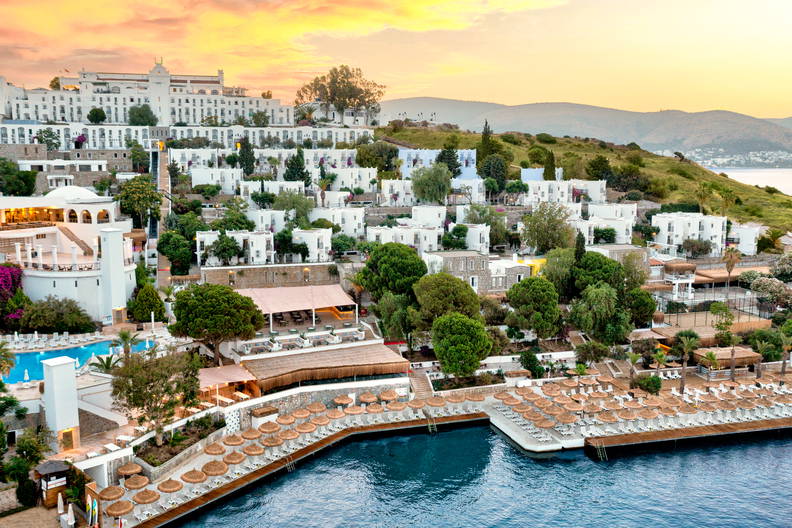 Nadmorski kurort z białymi budynkami, plażą i morzem w promieniach zachodzącego słońca.