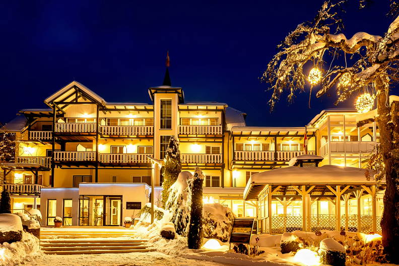Oświetlony zimą hotel z balkonami pokrytymi śniegiem.