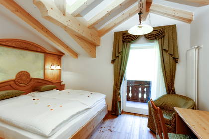 Pokój hotelowy z drewnianym łóżkiem, balkonem i drewnianą więźbą dachową.