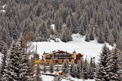 Zimowy widok na oświetlony Hotel des Alpes, otoczony ośnieżonym lasem.
