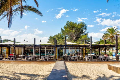 Restauracja na plaży z drewnianym pomostem i palmami.