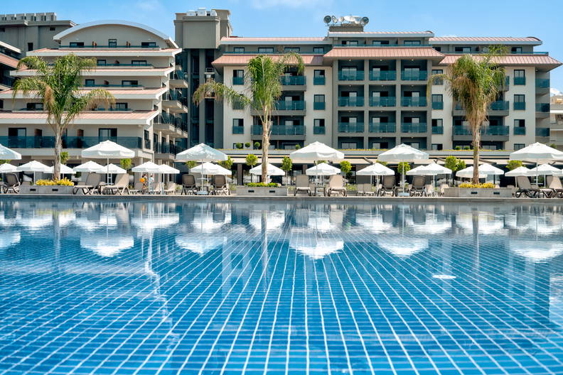 Błękitny basen, w którym odbijają się parasole i budynek hotelu.