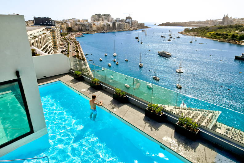 Mężczyzna pływa w basenie na dachu budynku z widokiem na zatokę i miasto.