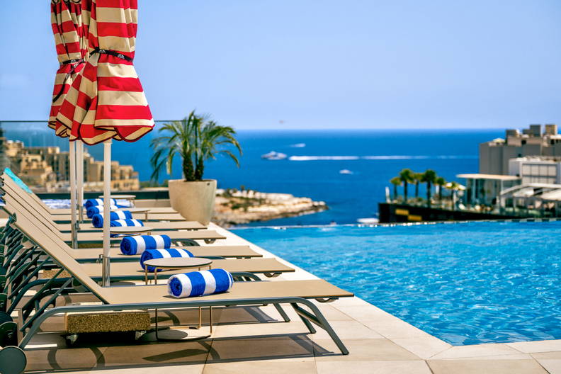 Leżaki z ręcznikami przy basenie z widokiem na morze.