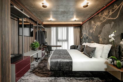 Pokój hotelowy w neutralnych kolorach z łóżkiem, biurkiem i szafą.