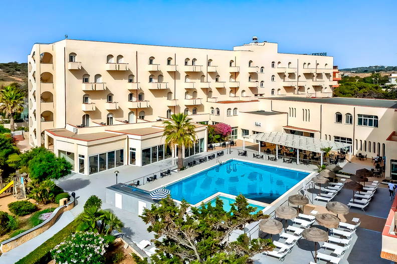 Duży, kilkupiętrowy hotel z basenem otoczonym leżakami i parasolami.