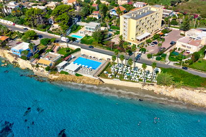 Widok z lotu ptaka na hotel z basenem i leżakami, tuż przy plaży i turkusowym morzu.