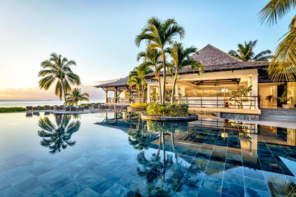 Luksusowy hotel z basenem i palmami nad oceanem o wschodzie słońca.