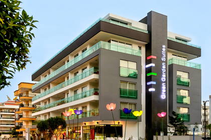 Nowoczesny budynek hotelu Green Garden Suites o zmierzchu, z kolorowymi, świecącymi dekoracjami w kształcie kwiatów.