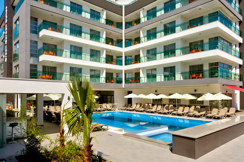 Basen z leżakami i parasolami na dziedzińcu nowoczesnego hotelu.