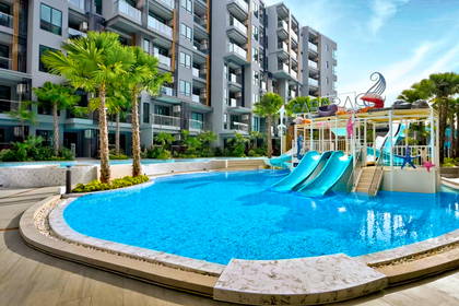 Basen z niebieskimi zjeżdżalniami na tle nowoczesnego apartamentowca i palm.
