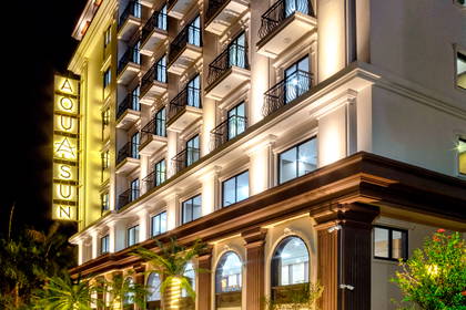 Nocą oświetlony hotel Aquasun z pionowym neonem i palmami ozdobionymi lampkami.