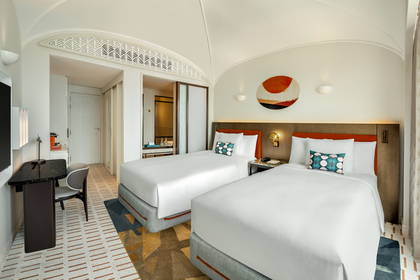 Nowoczesny pokój hotelowy z dwoma pojedynczymi łóżkami, biurkiem i abstrakcyjnym obrazem na ścianie.